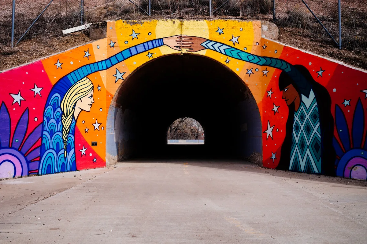 Colorful "Build Bridges, Not Walls" mural of two women reaching across a tunnel entrance to join hands above a path