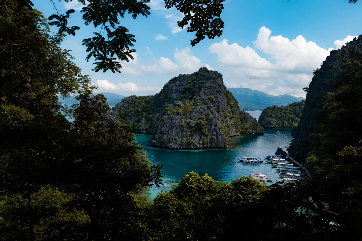 View through jungle trees of turquoise water, limestone karst islands and moored boats in Coron, Palawan, Philippines