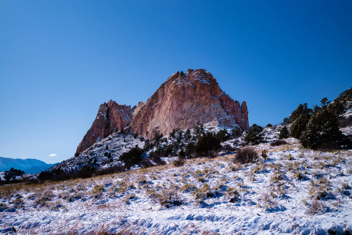 Red sandstone rock formation rising above snowy grassland under a deep blue sky at Garden of the Gods, Colorado Springs