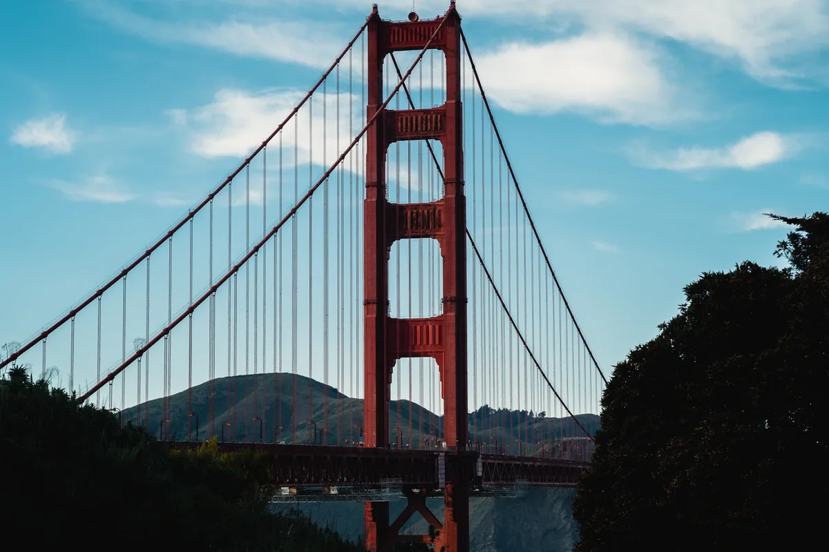 Red tower and suspension cables of the Golden Gate Bridge against a blue sky with green hills behind, San Francisco