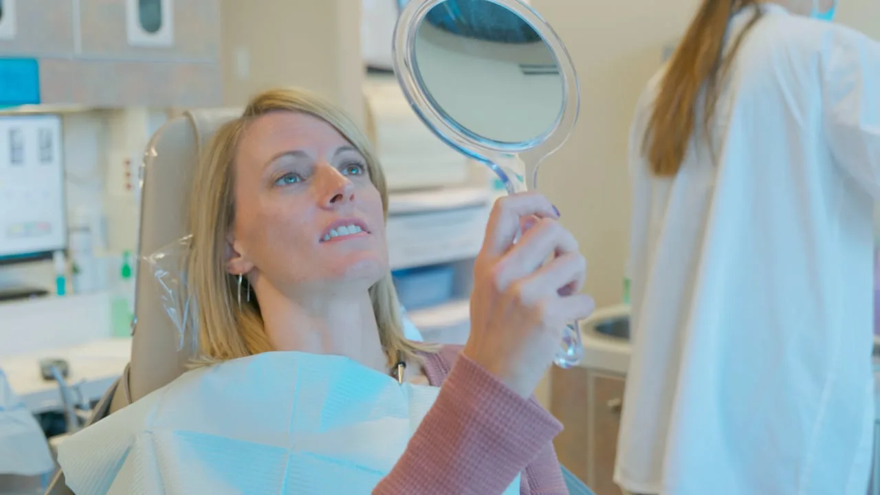 Still from a film for Peak Dental Health: a woman in a dental chair checks her smile in a hand mirror as an assistant stands by