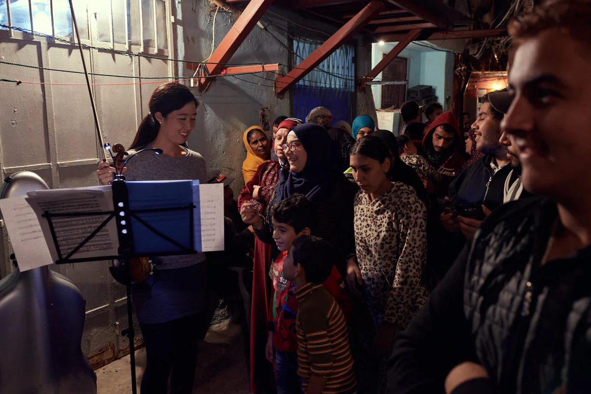 A smiling violinist faces women, children and young men gathered in an alley of Said Gawash camp, Beirut