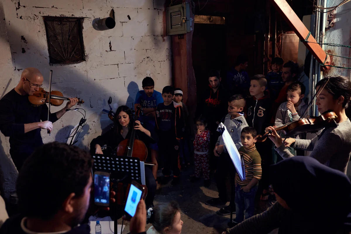 Cellist Ani Kalayjian and two violinists play in a narrow alley of Said Gawash camp, Beirut, as children crowd in to watch