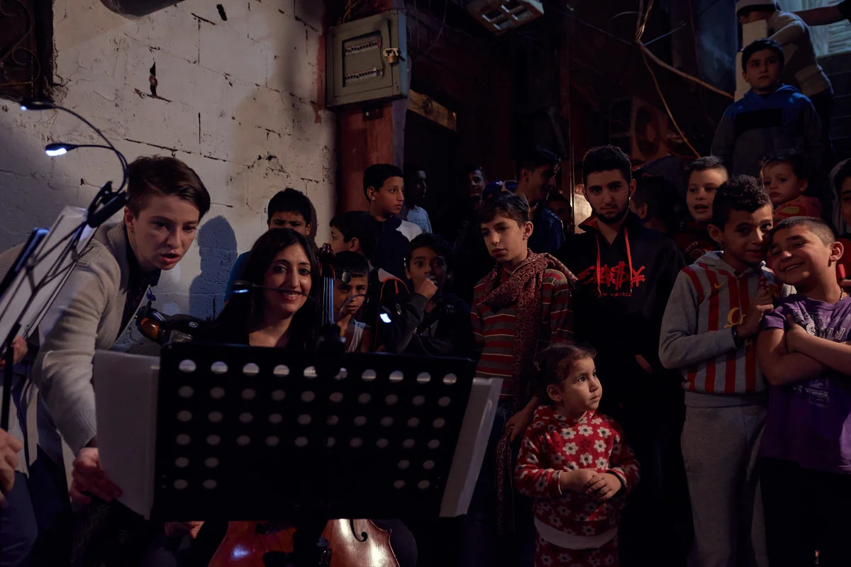 Mezzo-soprano Kristin Gornstein sings beside cellist Ani Kalayjian as a small girl and boys watch in Said Gawash camp, Beirut