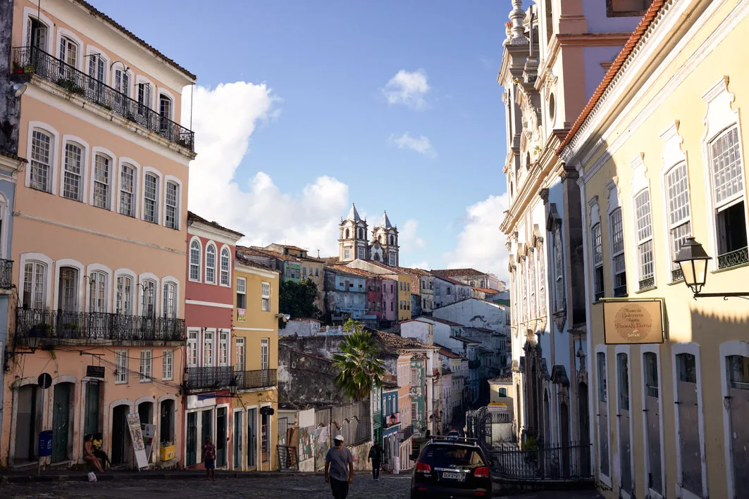 Pastel colonial houses with iron balconies line a cobbled street toward twin church towers in Salvador's old center