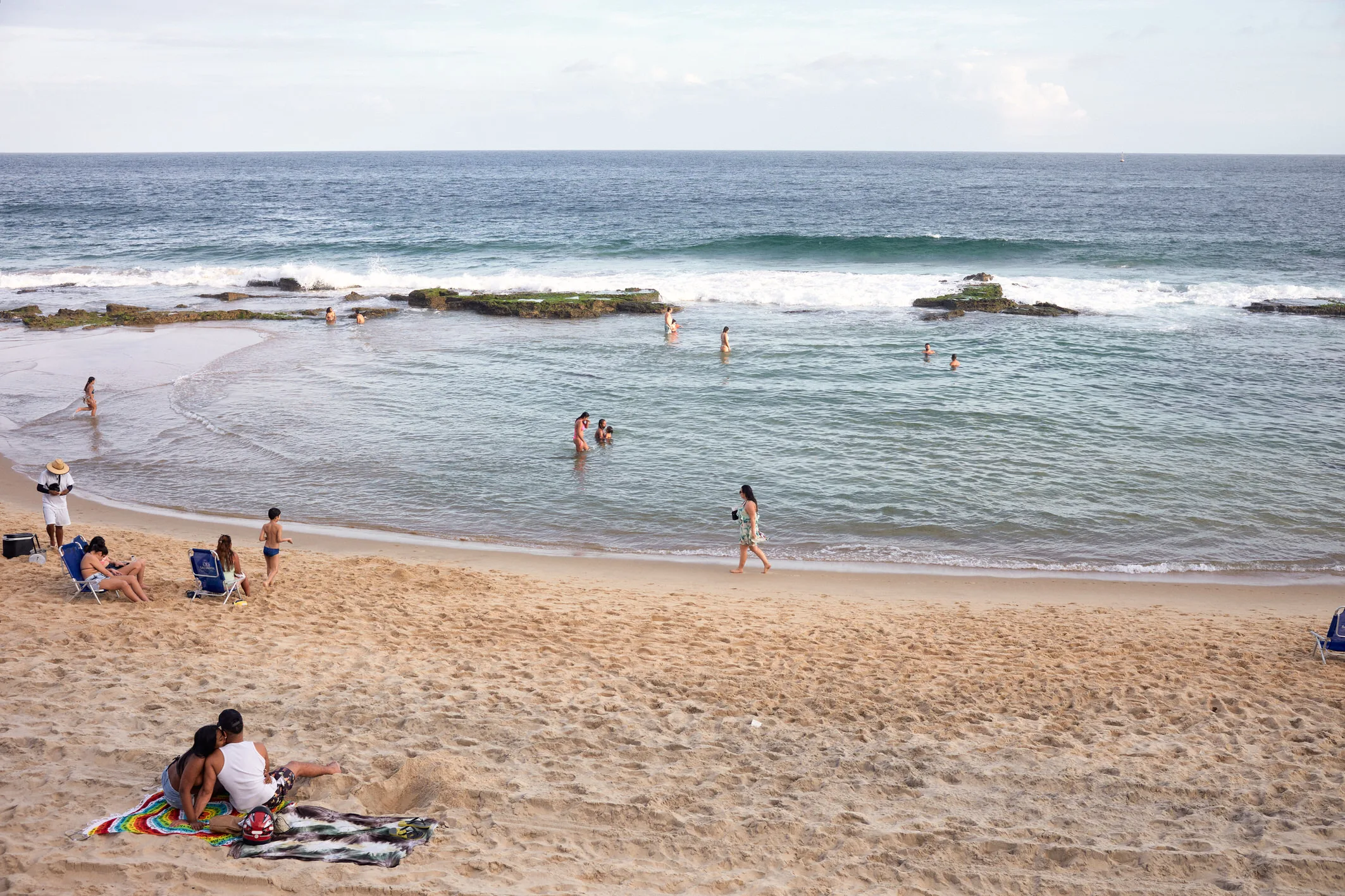 Bathers wading in the shallows and couples on towels on the sand at Barra beach on a soft afternoon, Salvador, Bahia