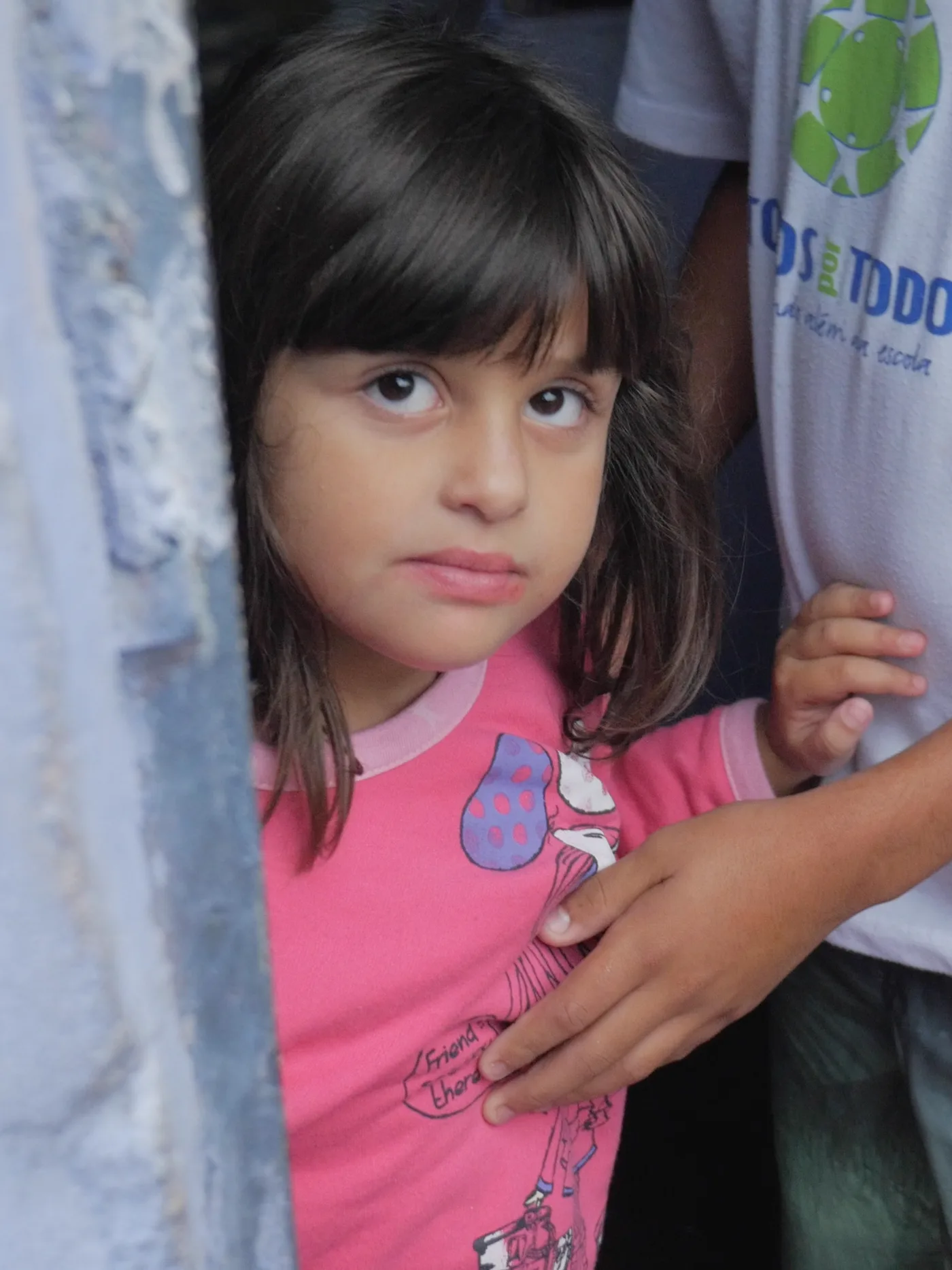 A girl at a doorway beside an older boy in a Todos por Todos shirt, Belo Horizonte