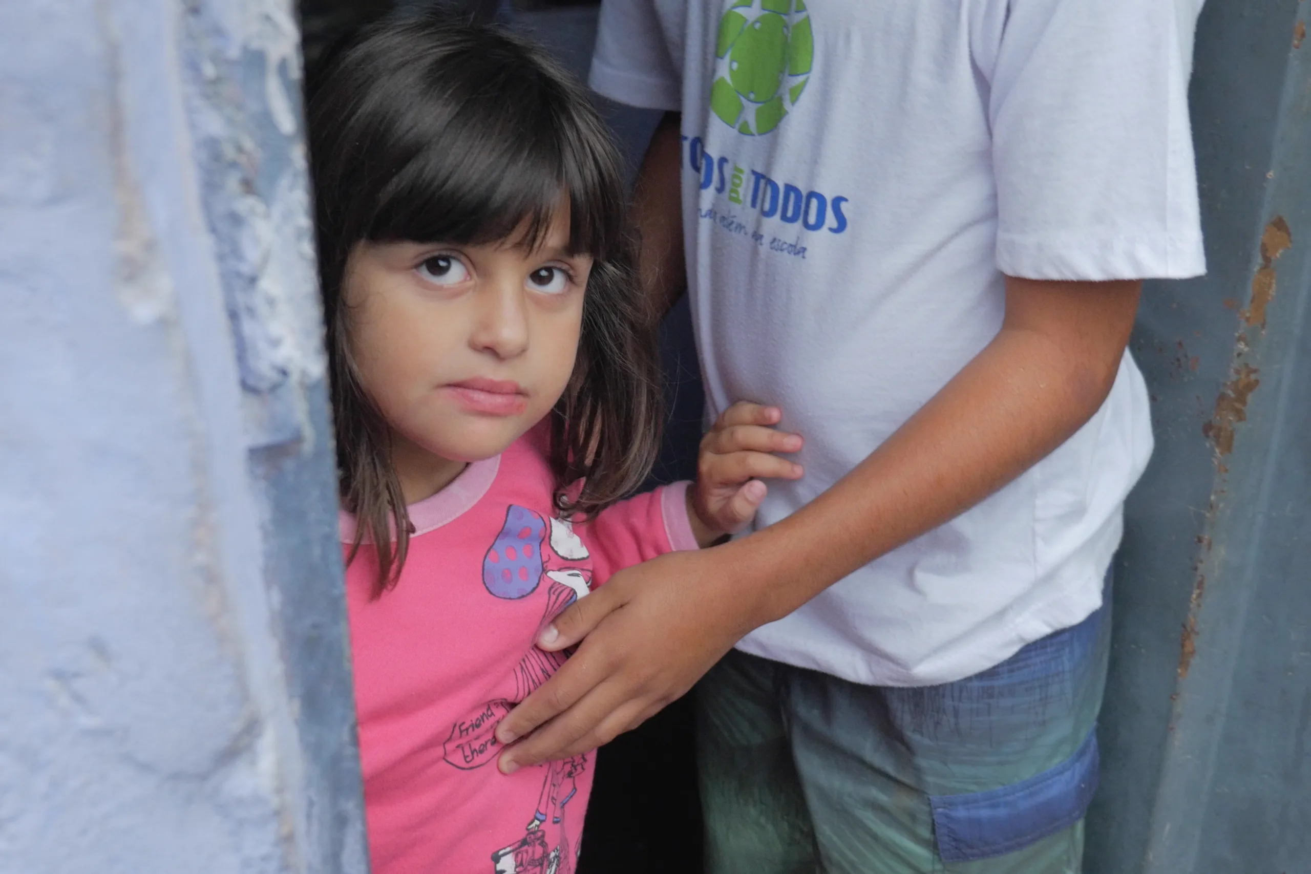 A girl at a doorway beside an older boy in a Todos por Todos shirt, Belo Horizonte