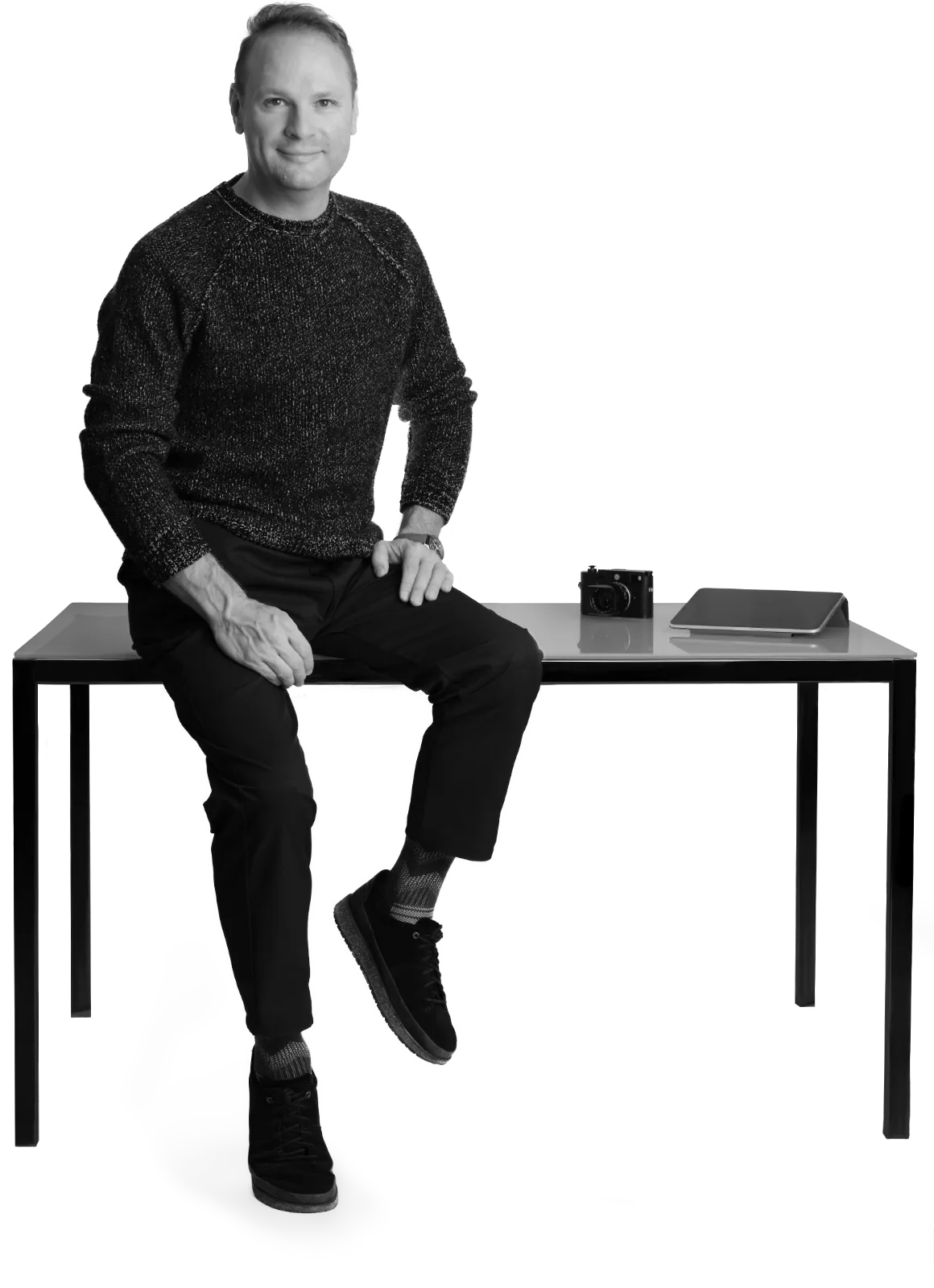 Alejandro Gomez-Meade sitting on a desk with an iPad and a Leica camera