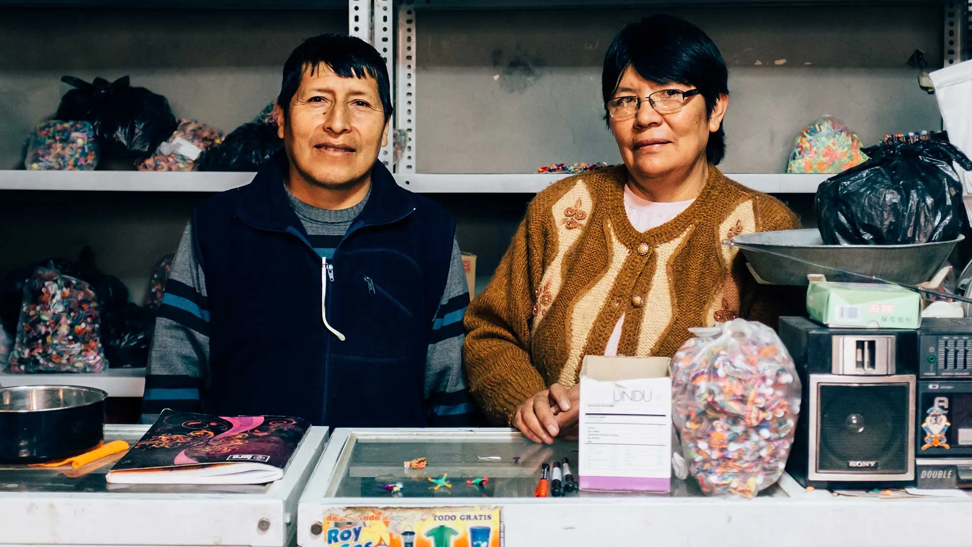 Cover of Meet the Artisans: Captcha: a man and a woman stand behind a shop counter with bags of colorful craft pieces