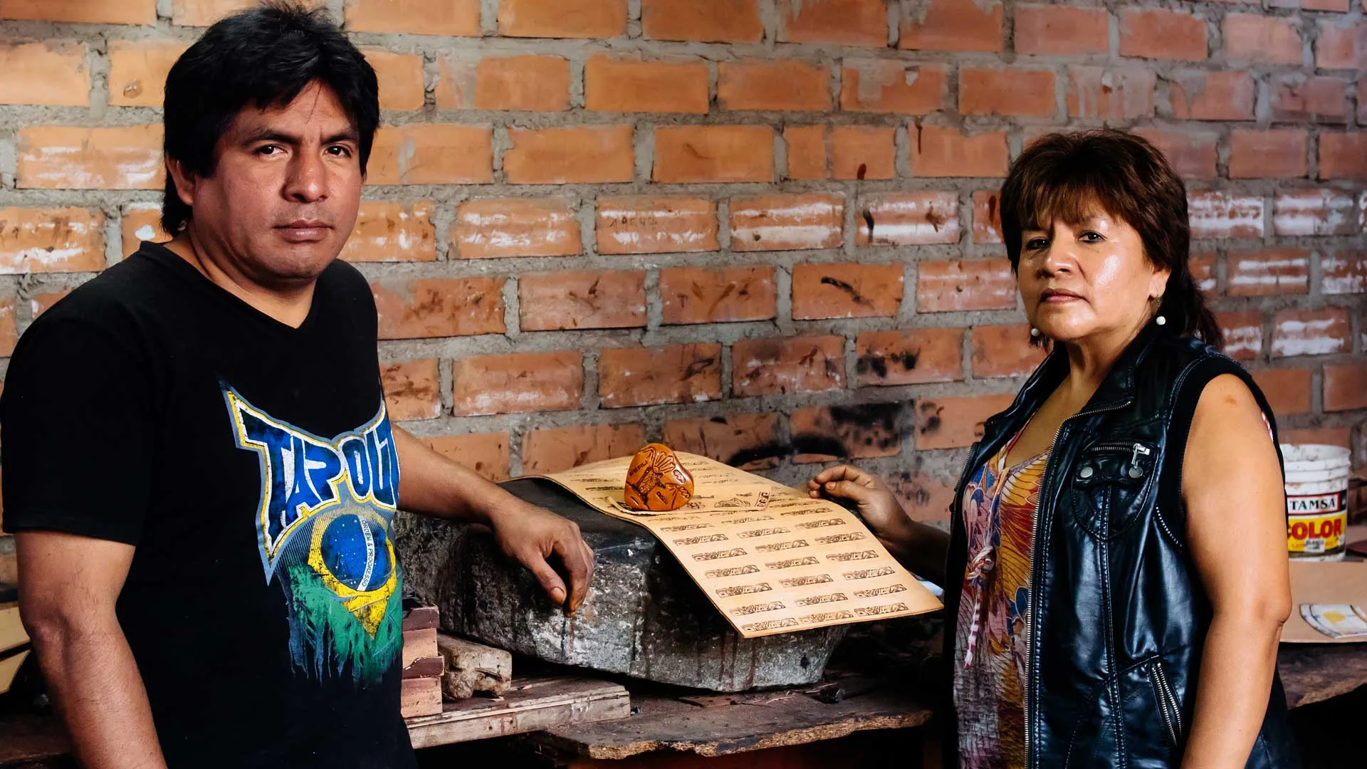 Cover of Meet the Artisans: Maria: a man and a woman stand at a brick wall by an engraved gourd on a sheet of carved patterns
