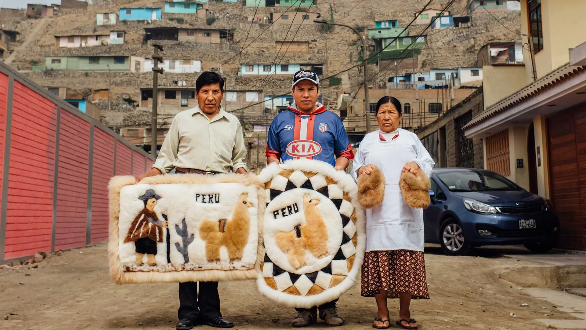 Cover of Meet the Artisans: Pacompilla: three artisans hold llama-pattern fur rugs and slippers on a hillside street in Peru
