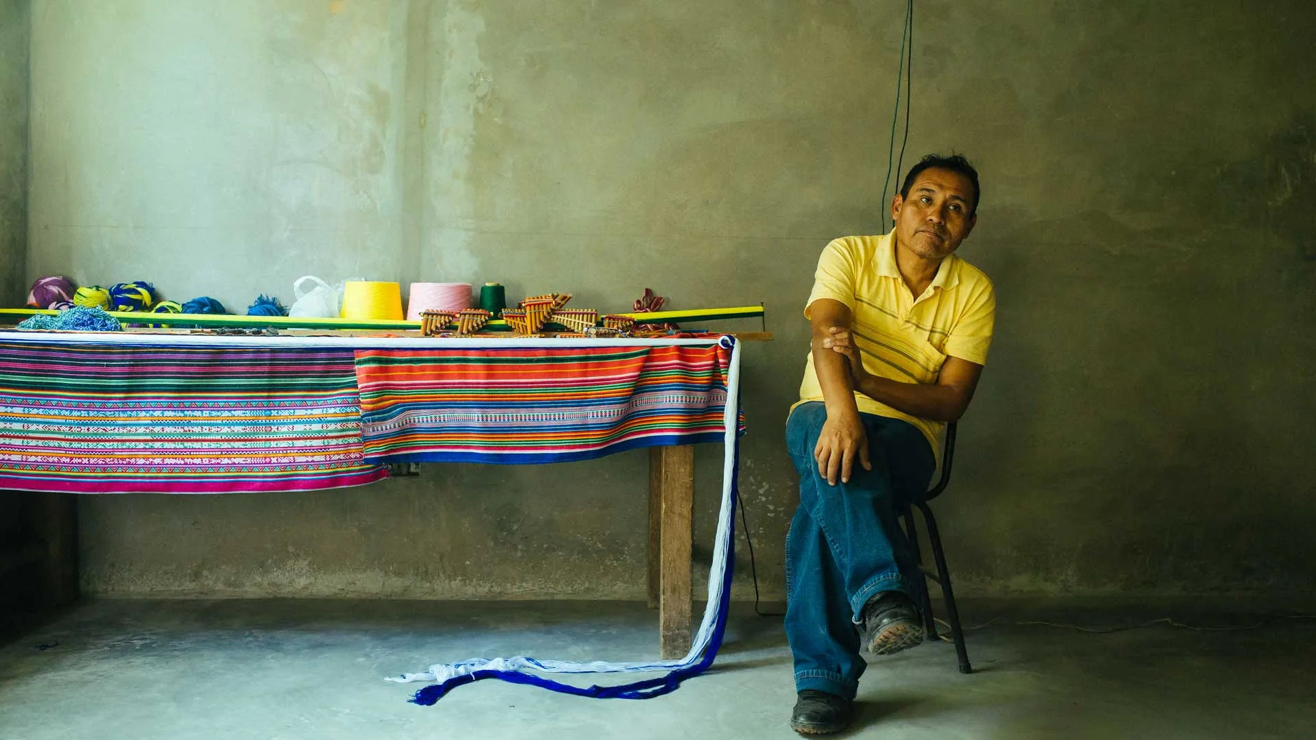 Cover of Meet the Artisans: Silverio Wanka: Silverio Wanka sits beside a table of striped woven cloth, yarn and panpipes