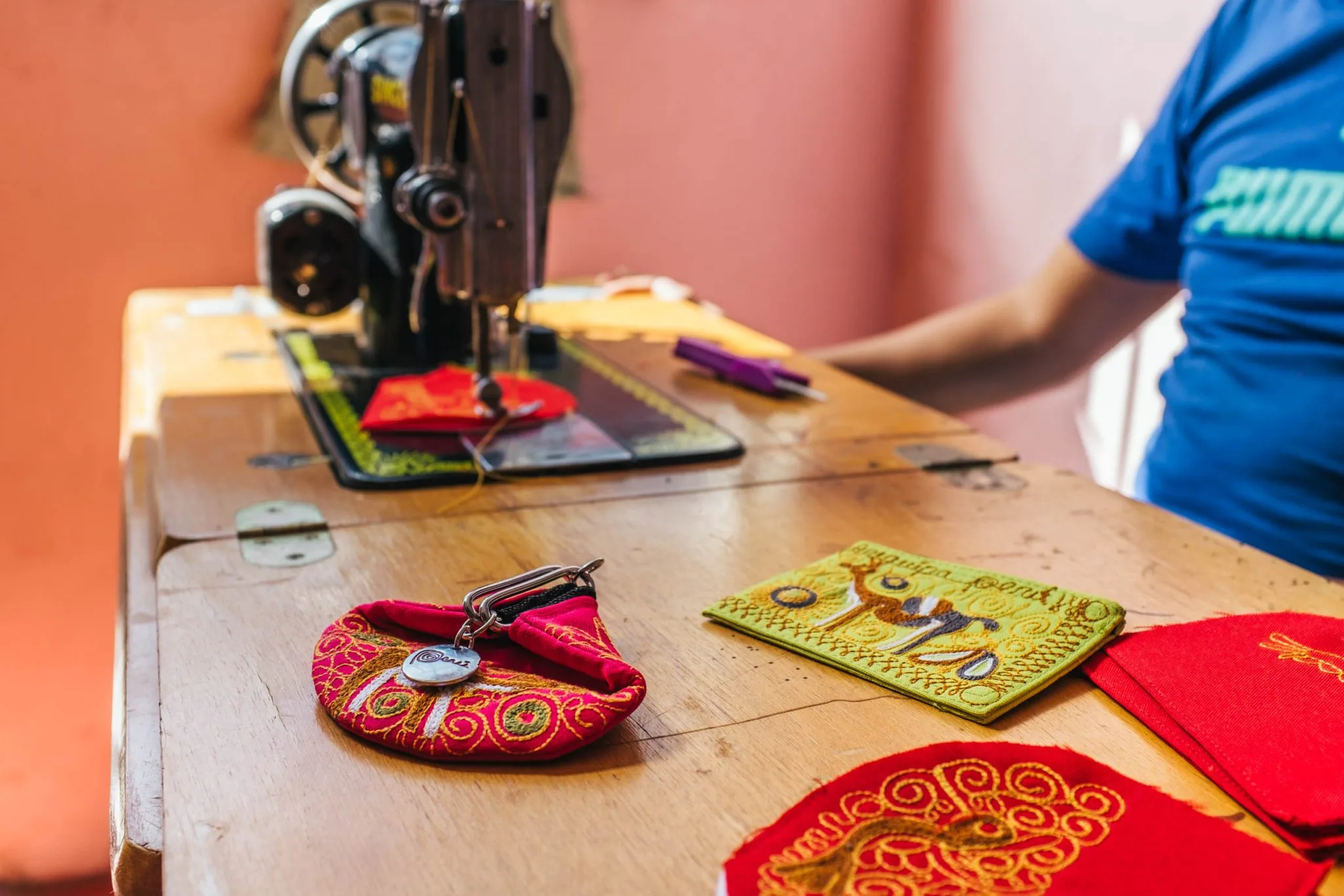 Embroidered coin purse and patches in red and green on a wooden sewing-machine table, a Singer machine behind