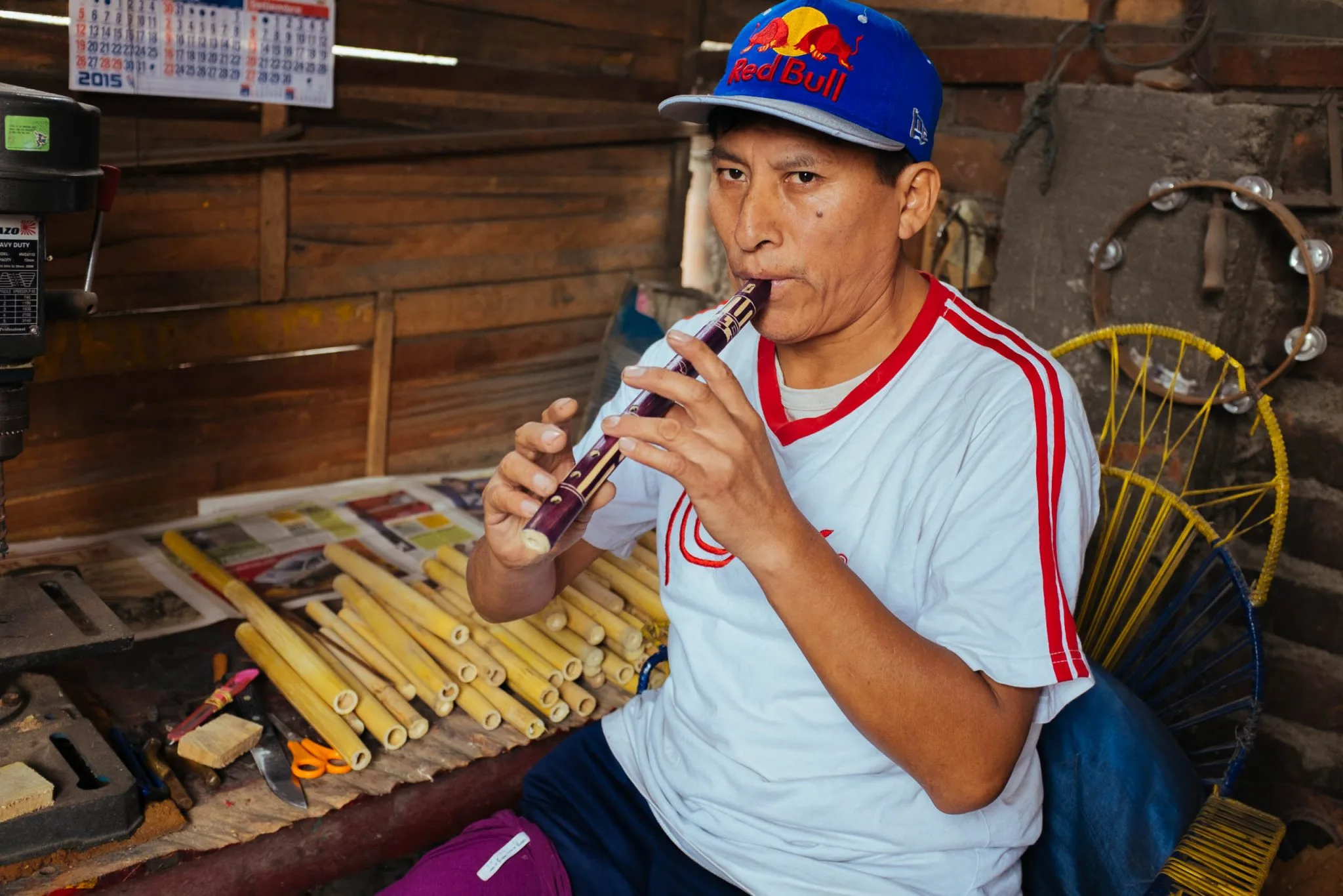 Cispe plays a cane flute he made, cut cane tubes on the bench beside him