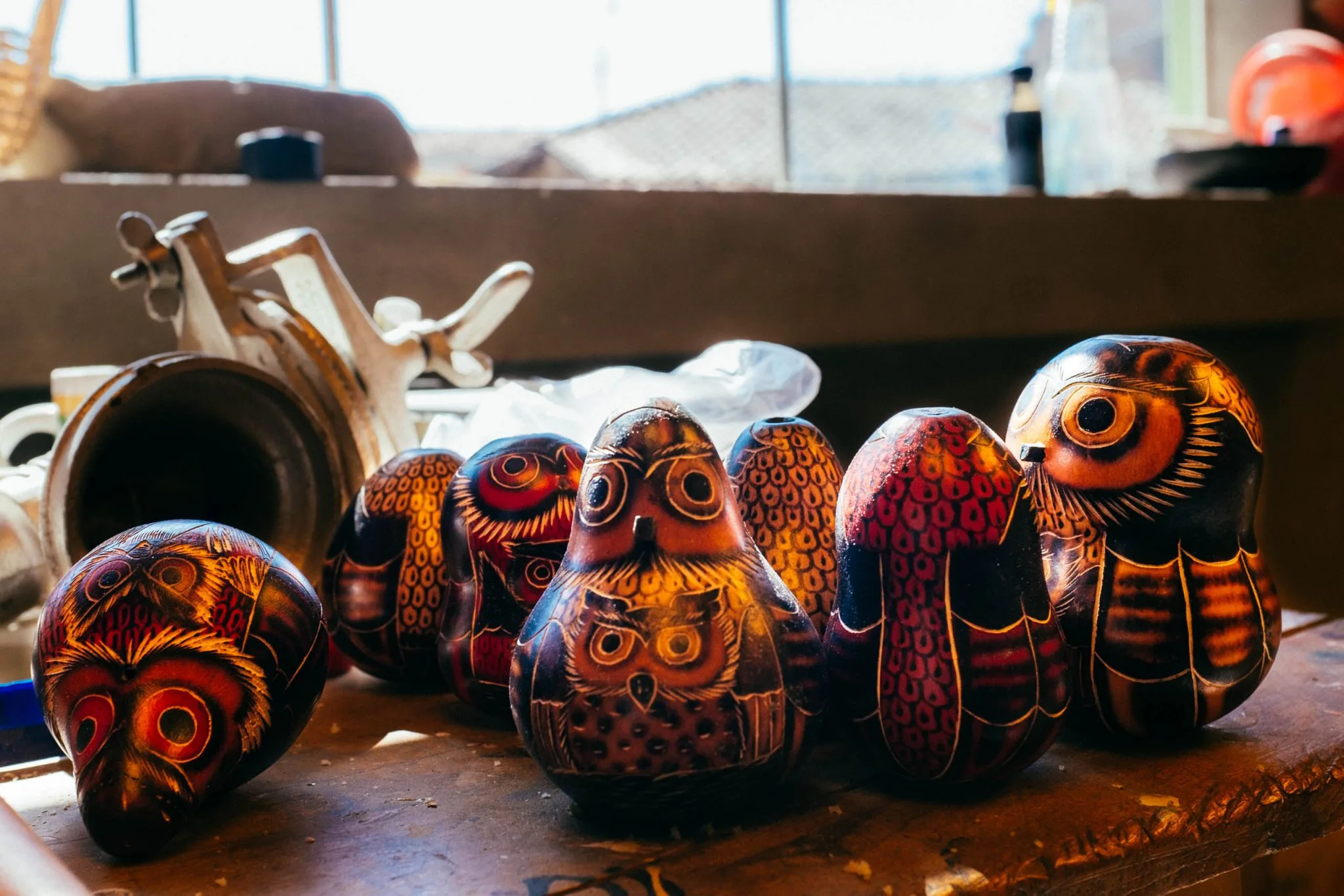 Carved and burned gourds shaped as owls on a workbench by a sunlit window