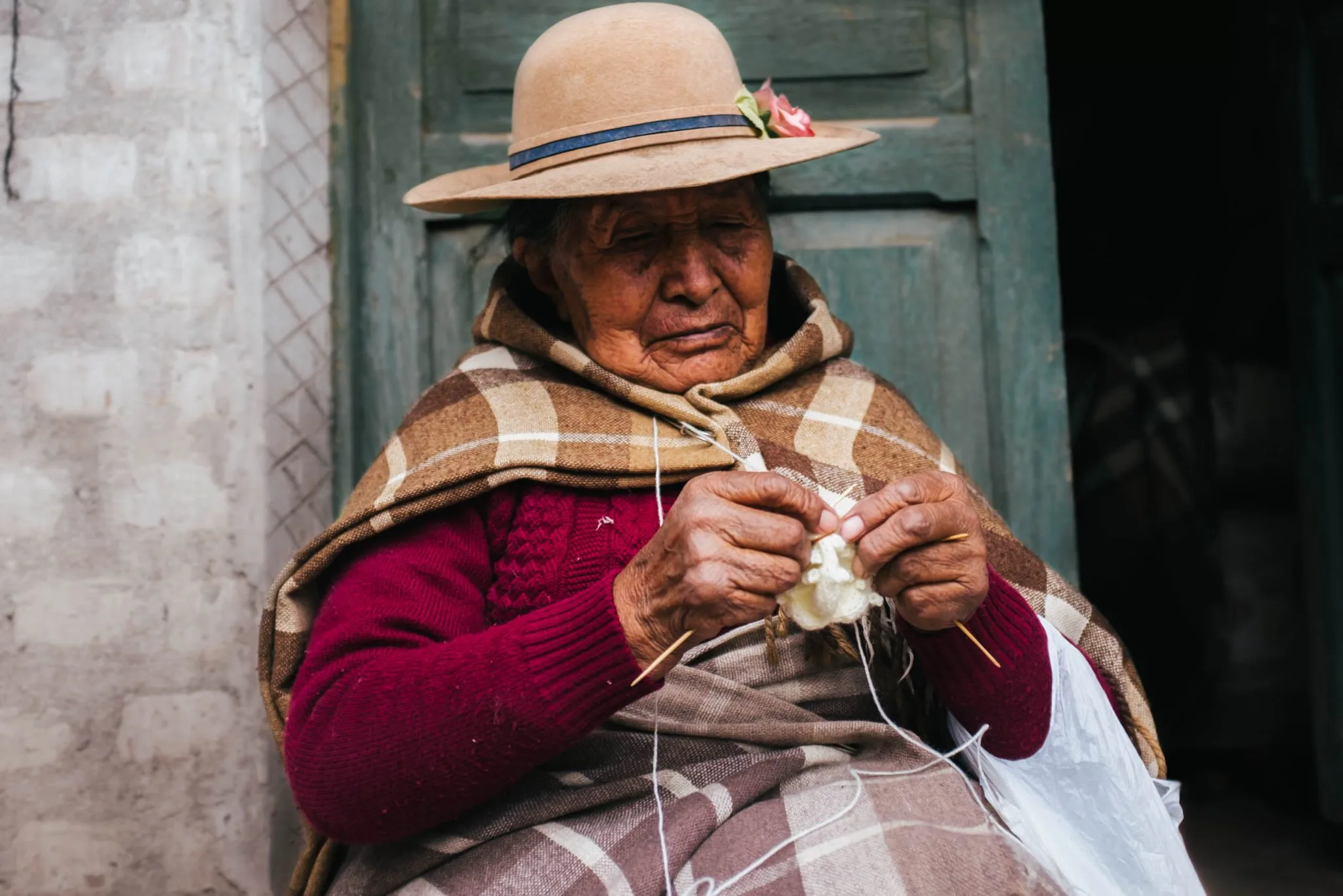 Mabel’s grandmother, in a wide-brimmed hat and a plaid shawl, knitting white yarn by a green doorway