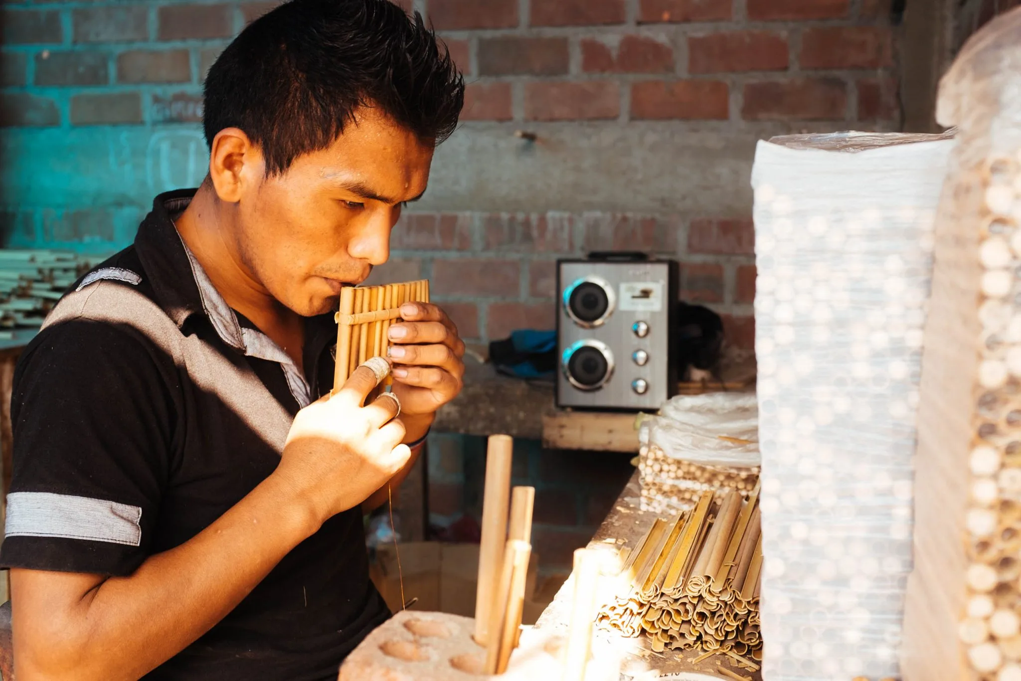 Silverio Wanka’s son tries a set of cane panpipes in his workshop, cut cane stacked beside him
