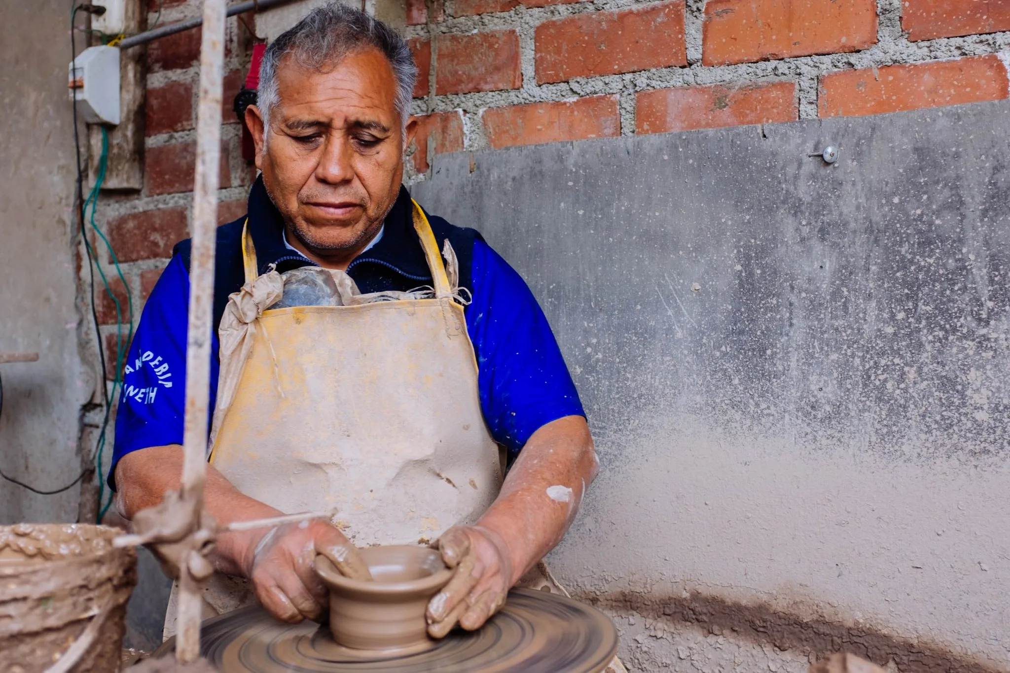 Potter José Yaksa shapes a small bowl at his wheel in his brick workshop