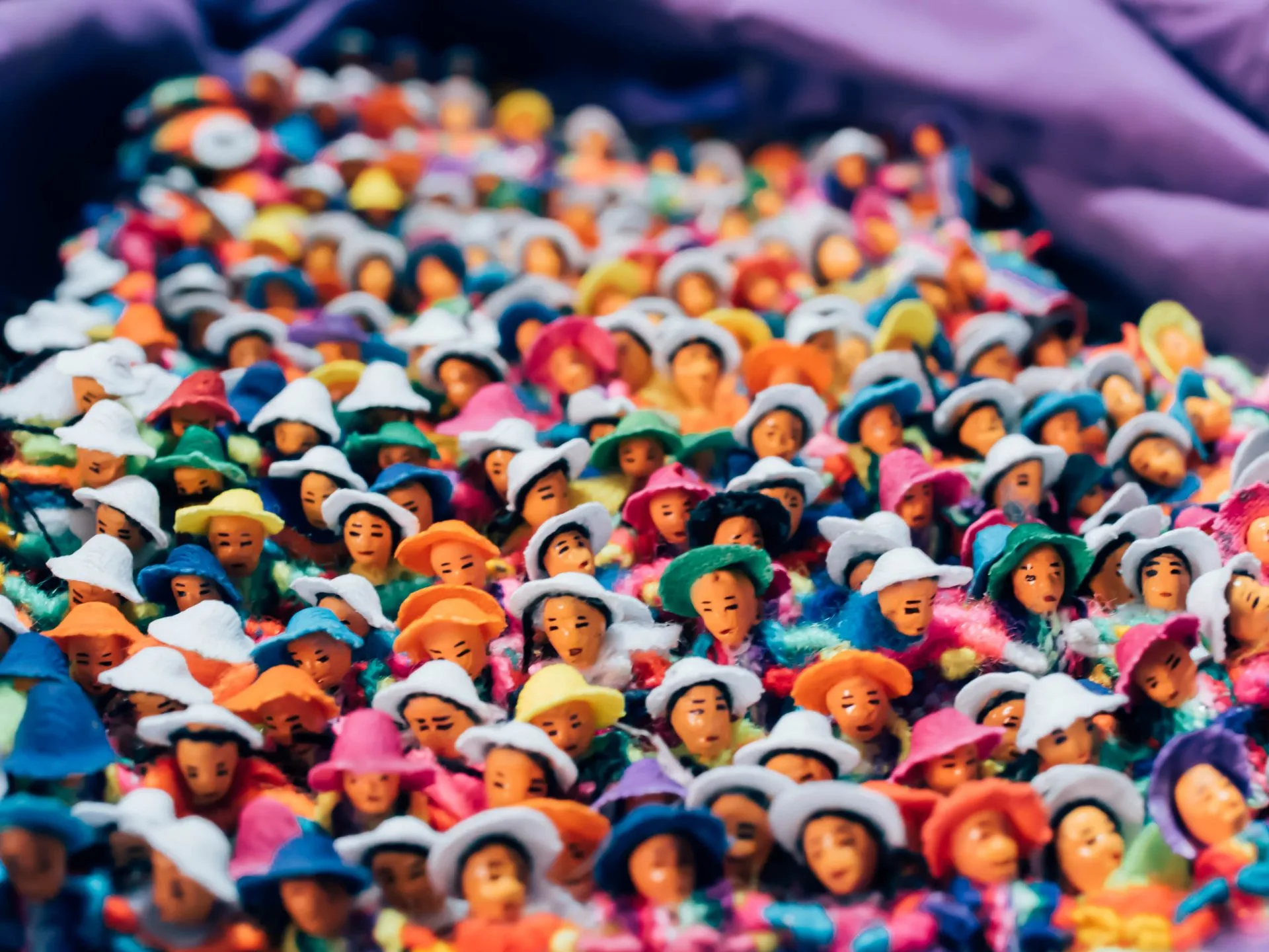 Hundreds of tiny handmade worry dolls in colored hats heaped on purple cloth